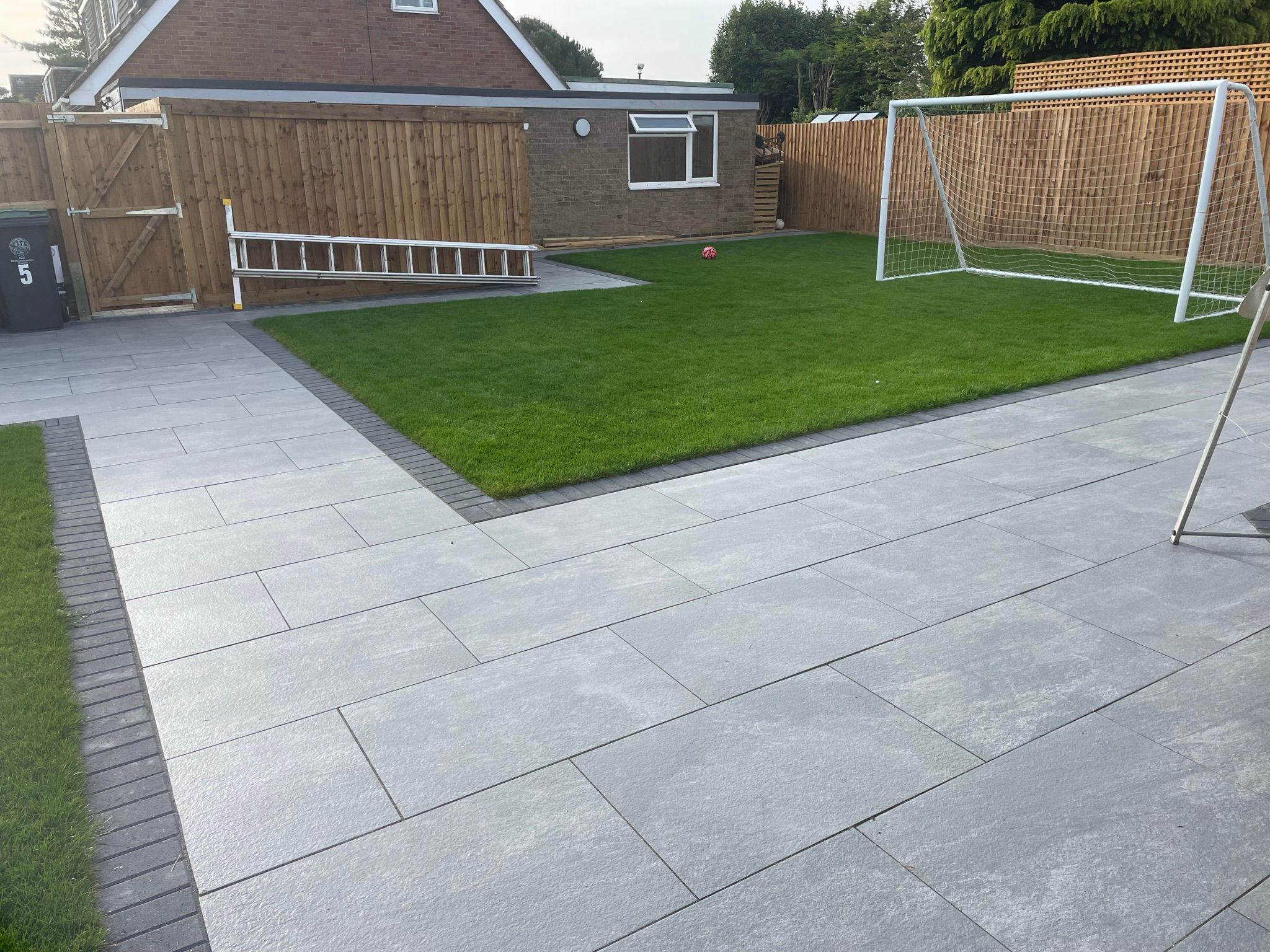 This is a photo of a patio installed using porcelain paving slabs with a dark grey brick border.